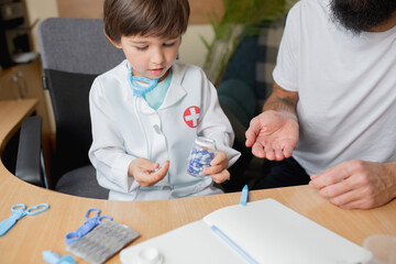 Little boy playing pretends like doctor examining a man in comfortabe medical office. Healthcare, childhood, medicine, protection and happiness concept. Having fun, laughting while giving pills