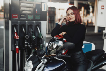 A joyful female biker enjoying her motorcycle. A modern bike and its female owner in the refueling. Retro styled photo.