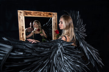 Obraz premium beautiful girl in an angel costume with black wings and a handsome man near the mirror on a black background