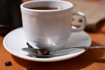 poured black coffee into a white cup near the turk and coffee grains on burlap and wooden table.