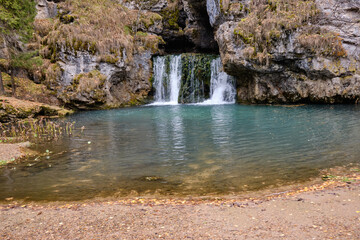 a small waterfall in the autumn forest flows out of the rock