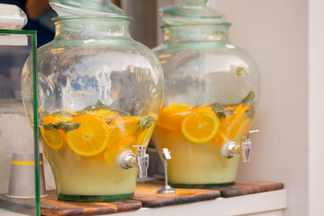 Refreshing drink: vintage pitcher of homemade lemonade, mojito cocktail with mint and orange slices on table at outdoor summer local food market