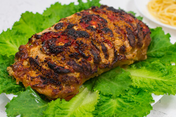 A large piece of chopped pork meat, cooked in the oven, baked in the oven, on green lettuce leaves, close-up.