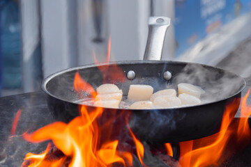 Process of cooking scallop meat on frying pan with hot flames at summer outdoor food market: close up. Seafood, barbecue, gastronomy, cookery, street food concept