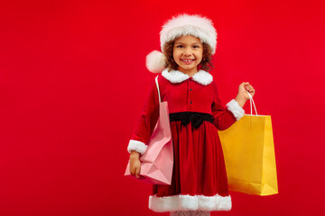 A little African American girl in a Santa hat and with a carrier bags is happy to go shopping