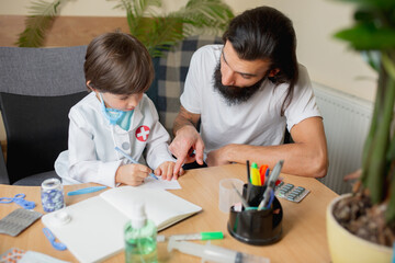 Obraz na płótnie Canvas Little boy playing pretends like doctor examining a man in comfortabe medical office. Healthcare, childhood, medicine, protection and happiness concept. Having fun, laughting while giving pills recipe