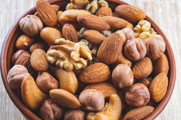 a mixture of nuts in a clay plate on a wooden table, a concept of healthy food, top view