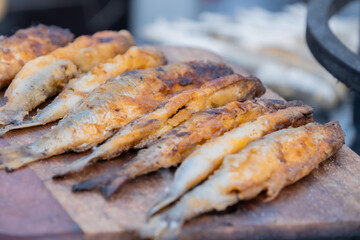 Crispy breaded european smelt fish on wooden cutting board at summer outdoor food market: close up. Seafood, barbecue, gastronomy, cookery, street food concept
