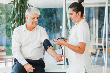 Fototapeta premium mexican woman doctor examining blood pressure to senior patient in medical clinic in Latin America