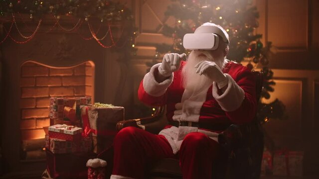 Santa Claus is using VR headset, swiping by hands in air, sitting alone in room at Christmas night