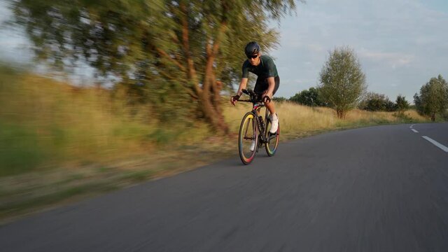 Portrait of cyclist man training on road bike. Healthy man riding bicycle and working outdoors at the sunset.