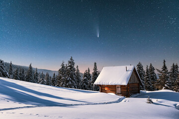 Fantastic winter landscape with wooden house in snowy mountains. Starry sky with comet and snow...