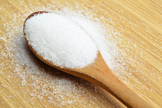Granulated sugar in wooden spoon on bamboo cutting board, on bamboo cutting board