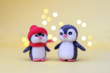 Two woolly toy penguins on a yellow background with bokeh