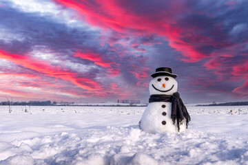 Funny snowman in stylish hat and black scalf on snowy field during sunset. Epic sky with purple...
