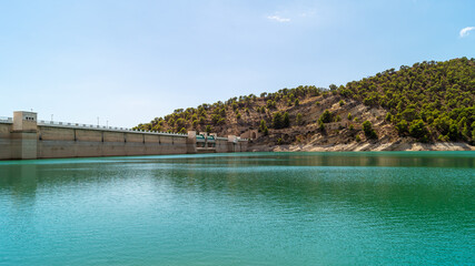 Fototapeta na wymiar Landscape in which you can see the wall of the Amadorio reservoir in Villajoyosa with the turquoise water and the mountains with wild vegetation that surrounds it (Spain). Sunny summer day.