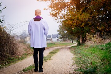 The figure of a priest from the back walking on a country road.