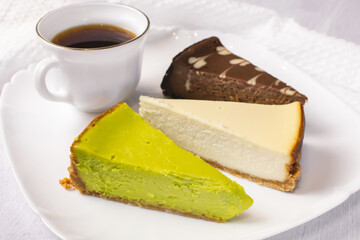 Set of New York, chocolate and pistachio cheesecake on white plate and cup of coffee