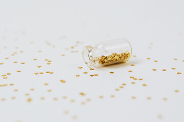 Spangles of gold and silver are scattered from bottles on a white background