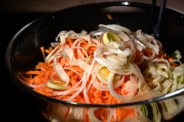 Healthy salad with carrot and leek in transparent bowl on dark background