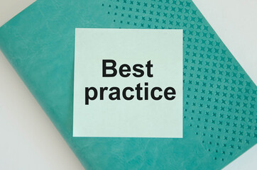 best practice text written on a blue sticker that is glued to a green notebook that lies on a white background