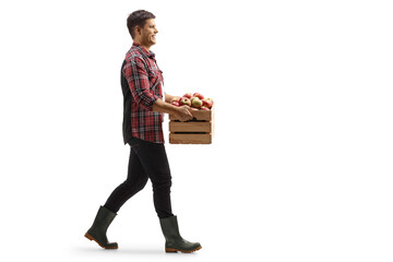 Full length profile shot of a young man walking and carrying a crate with apples