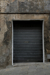 Ancient garage door with closed shutter, brick wall cracked, damaged and weathered, space for text on the blank shutter, perfect background for a gift card