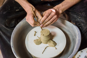 Professional male potter shaping mug with special tool in pottery workshop, studio. Crafting, artwork and handmade concept