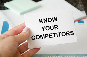 text know your competitors written on a white sheet of paper held by a business girl