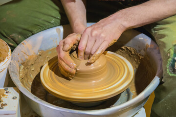 Professional male potter making pot on pottery wheel at workshop, studio - close up view. Handmade,...
