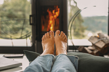 Woman barefoot relaxing in comfortable home, cozy warm moments. Feet at modern fireplace and window