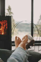 Woman barefoot relaxing in comfortable home, cozy warm moments. Feet at modern fireplace and window