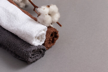 Multicolored towels and a branch of cotton on gray background.