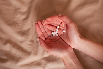 Woman holds in hand pills, vitamins, medicines over fabric texture. Outstretched hand with a handful of pills on the background

