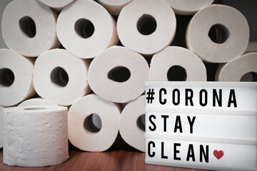 sign with the inscription #Corona stay Clean stands before a wall of toilet paper rolls