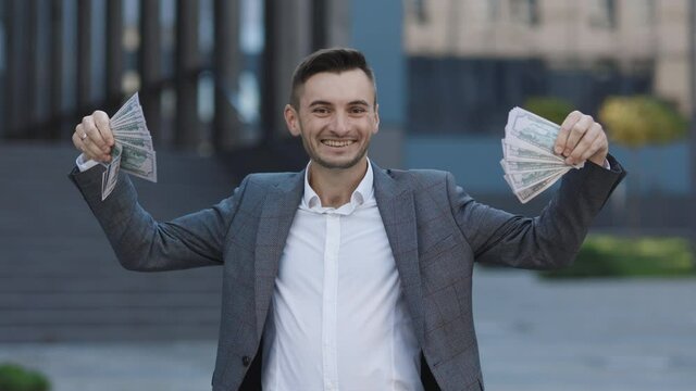 Amazed happy excited businessman with money - U.S. currency dollars banknotes. Man shows money and celebrating success, victory while looking to camera.