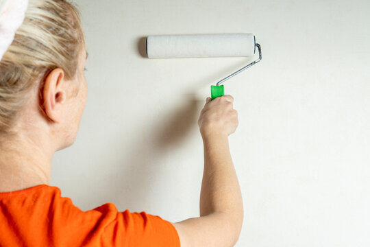 Girl with blond hair holds a paint roller smooth on a light background