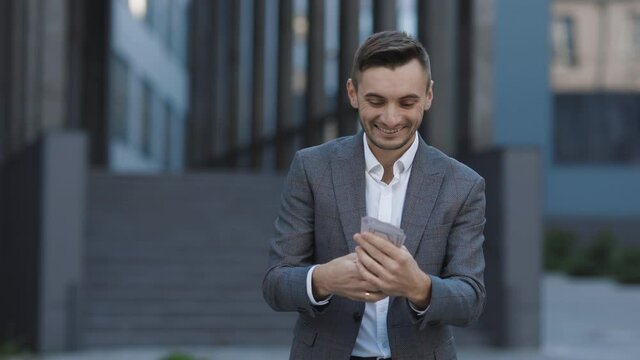 Lifestyle, richness, joy, success. Happy rich successful man holds dollars outdoors. Portrait of satisfied businessman holds money