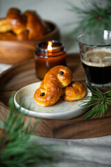 Two Swedish saffron buns (lussekatter), lit  candle and cup of coffee on wooden tray.