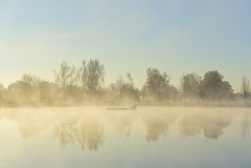 Romantic landscape in autumn, in the morning with rising haze over a lake and at sunrise