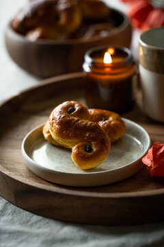 Two Swedish saffron buns (lussekatter), lit  candle and cup of coffee on wooden tray.