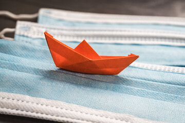 Orange origami boat sailing on a blue sea made with surgical masks.Pandemic problems concept, origami ship with surgical masks.