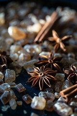 Close up brown sugar crystals, anise stars and cinnamon sticks on deep blue background.