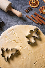 Rolling pin, flour, shapes for gingerbread, dough and cinnamon on cooking kitchen table. Christmas food preparation, view from above. Homemade bakery. Holiday cookies recipe. 