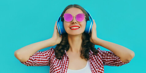 Portrait close up of smiling young woman in wireless headphones listening to music wearing a pink...