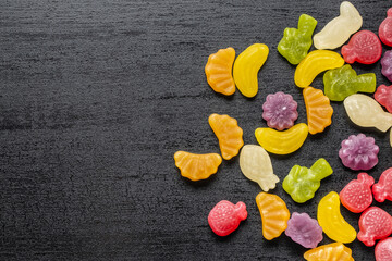 Colorful fruity jelly candies on black table.
