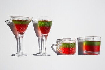 4 crystal glasses of different sizes in row with bright red and green filling inside on light background. Bright sun, cool interesting shadows. atmosphere of celebration and fun. Delicious desserts