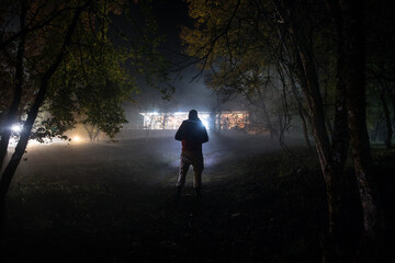 strange light in a dark forest at night. Silhouette of person standing in the dark forest with light. Horror halloween concept. strange silhouette in a dark spooky forest at night