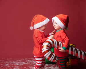 Obraz premium two toddler boys brothers twins in red Santa hat with Xmas candy cane on a red background.