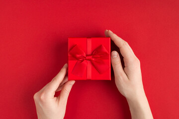 Valentine's day concept. Top above overhead view photo of female hands holding red giftbox with red ribbon isolated on red background